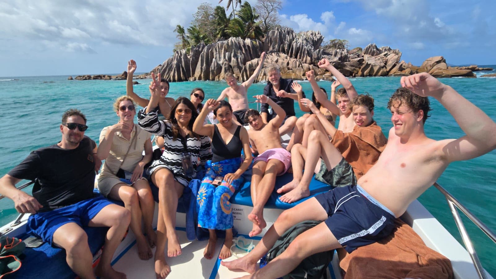 A full boat of guests cheering from the bow with the granite of St. Pierre behind them